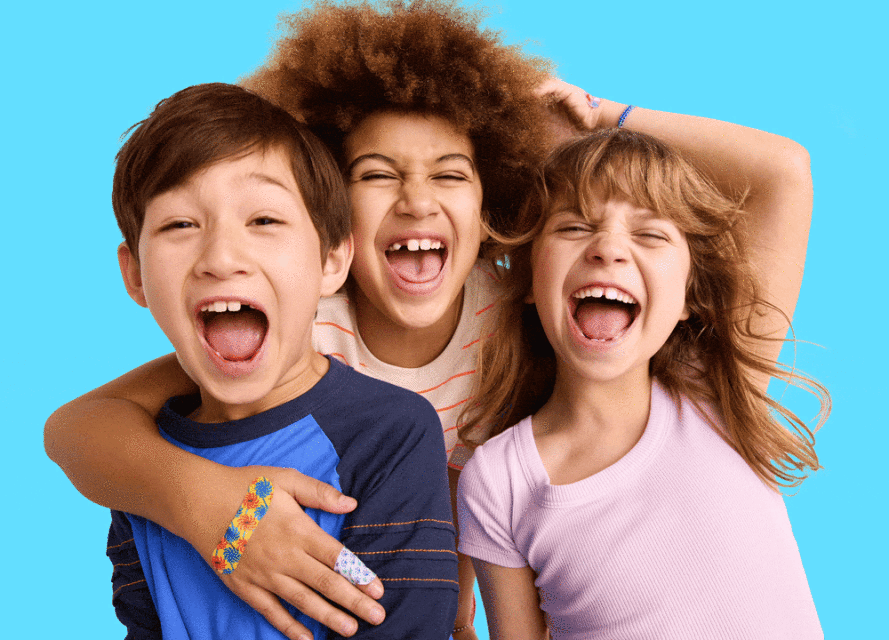 Three joyful children, two boys and a girl, embrace in a cheerful studio shot against a bright cyan backdrop. They are smiling and laughing.