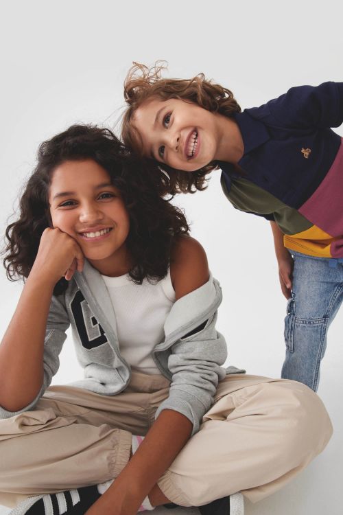 Two smiling children posing together against a plain white background, photographed by Priscilla Gragg.