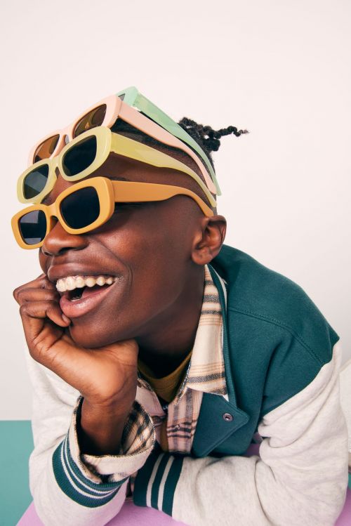 Smiling adult with sunglasses stacked on head in studio. The person wears a letterman jacket. Light and airy setting with playful feel.