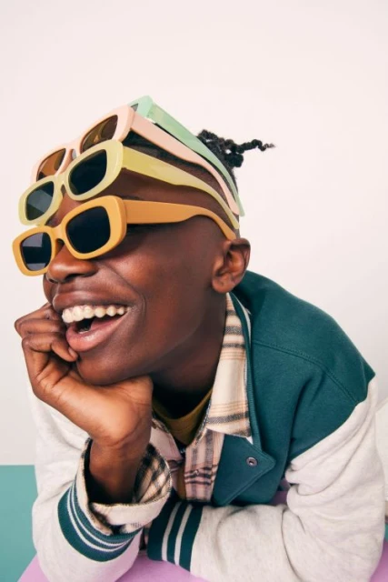 Smiling adult with sunglasses stacked on head in studio. The person wears a letterman jacket. Light and airy setting with playful feel.