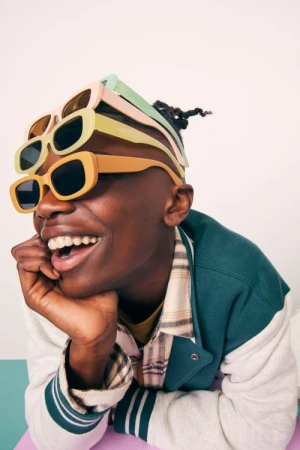 Smiling adult with sunglasses stacked on head in studio. The person wears a letterman jacket. Light and airy setting with playful feel.