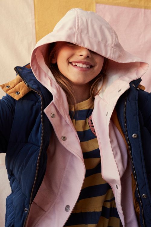 Smiling child wearing a navy blue puffer jacket and a pink bucket hat indoors in a close-up portrait.