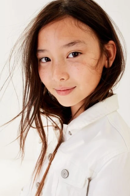 Portrait of a young girl with long brown hair wearing a white denim jacket against a white background in a head and shoulder view.