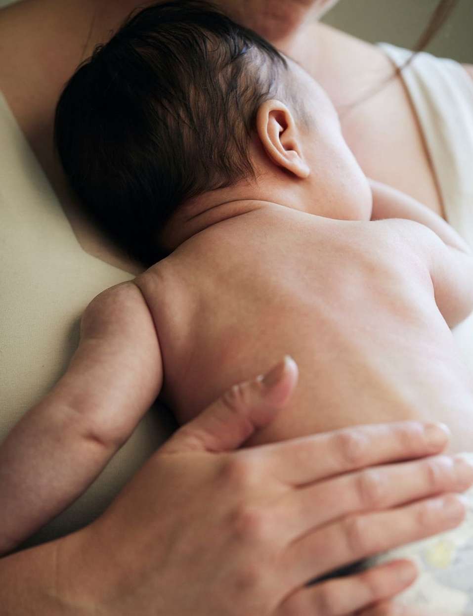 Close-up of baby lying on adult's chest, resting with arm extended, highlighting skin tones and family intimacy. Soft lighting.