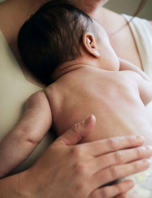 Close-up of baby lying on adult's chest, resting with arm extended, highlighting skin tones and family intimacy. Soft lighting.