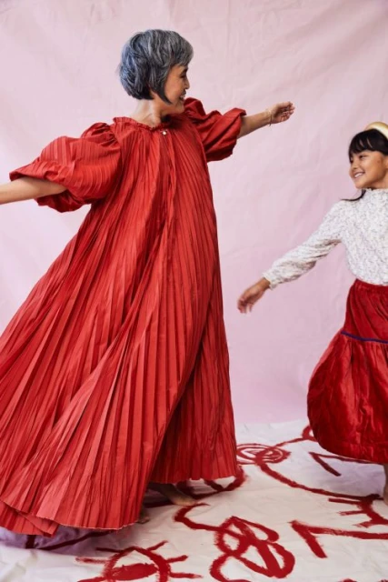 A joyful image features an adult woman and a child dancing together in red clothing against a pink background with abstract red drawings.