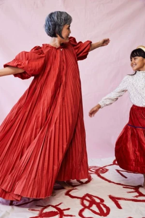 A joyful image features an adult woman and a child dancing together in red clothing against a pink background with abstract red drawings.