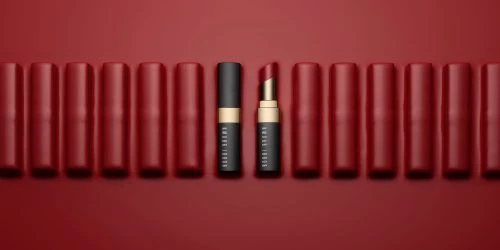 Beauty product shot of arranged red lipstick tubes and one partially open lipstick with gold trim on a red background.