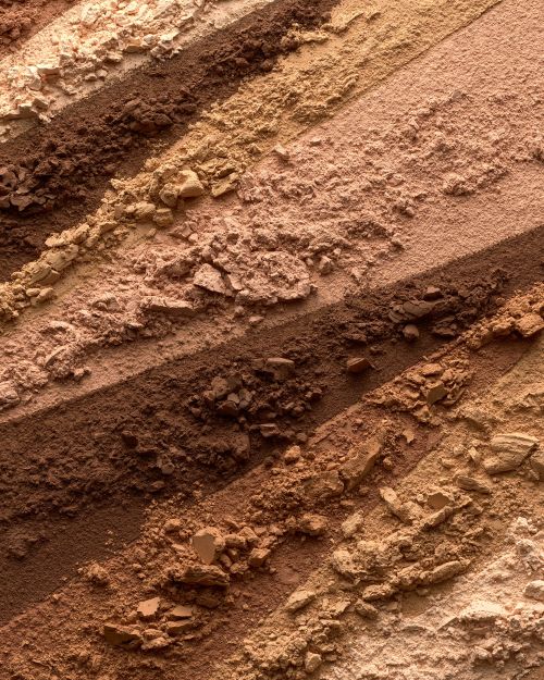 Close-up of multicolored, striated eyeshadow palette, showcasing light beige, tan, and brown shades in horizontal bands of loose powder.