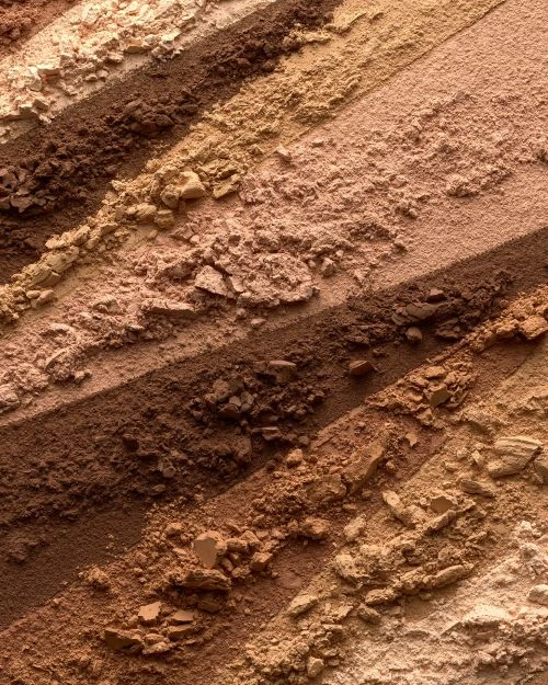 Close-up of multicolored, striated eyeshadow palette, showcasing light beige, tan, and brown shades in horizontal bands of loose powder.