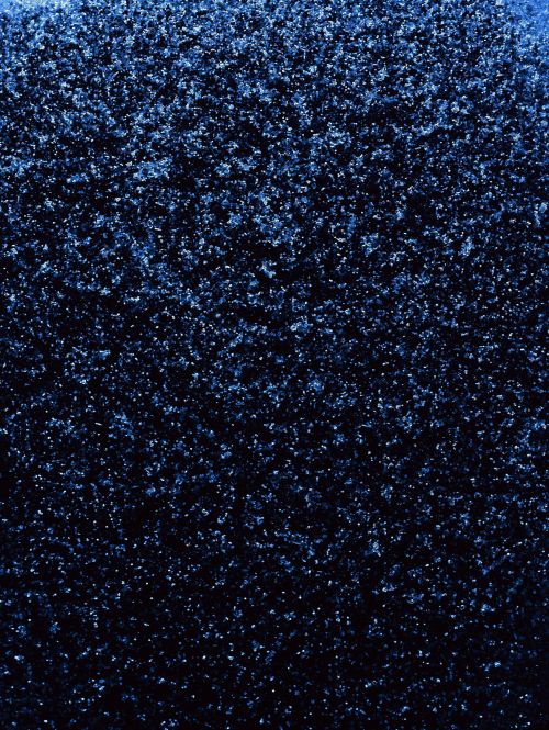 Close-up texture of a coarse, dark blue surface with scattered light-blue sparkles, creating a deep and shimmering effect.