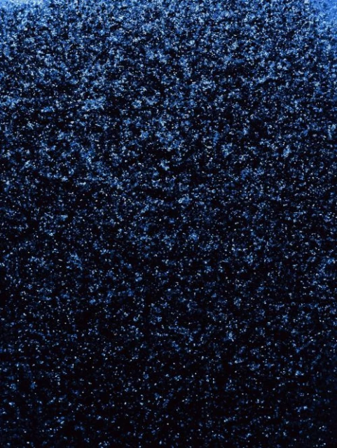 Close-up texture of a coarse, dark blue surface with scattered light-blue sparkles, creating a deep and shimmering effect.