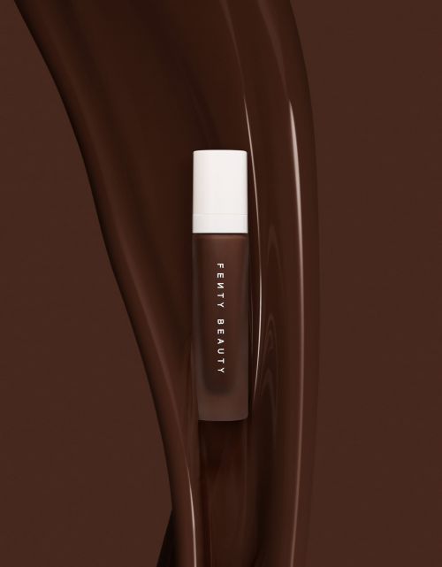 Fenty Beauty liquid cosmetic product bottle positioned vertically against a flowing rich brown liquid backdrop