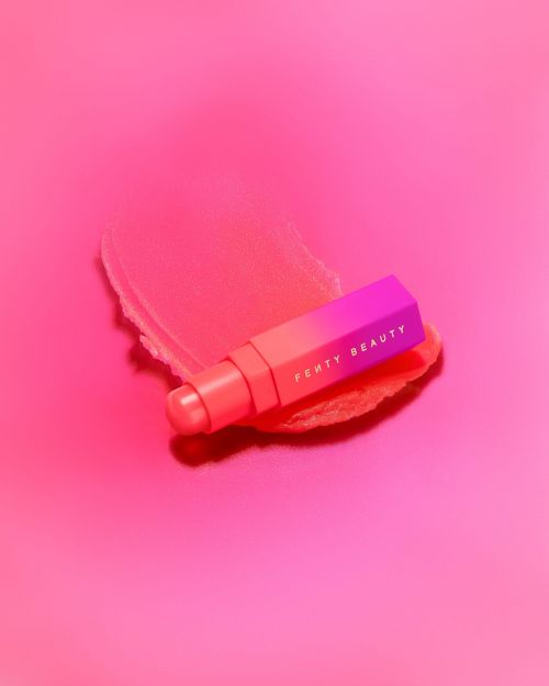 Fenty Beauty Match Stix on a pink surface, complemented by a swipe of product. Cosmetic presentation, highlighting product texture.