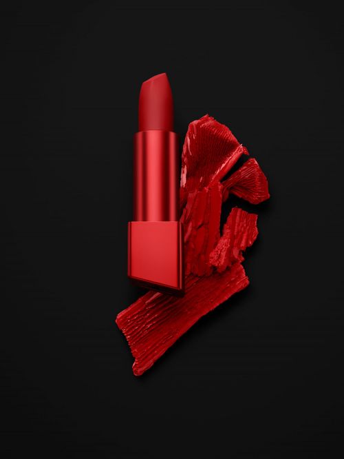 Red lipstick tube and smeared lipstick swatch on a stark black backdrop, showcasing beauty and cosmetic elegance.