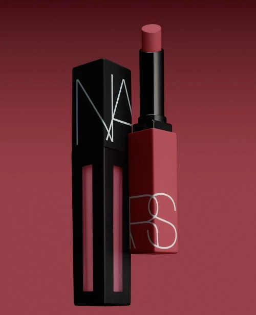 Two NARS brand lipsticks, one matte liquid lipstick in black packaging and one lipstick with a red tube, against a red background.