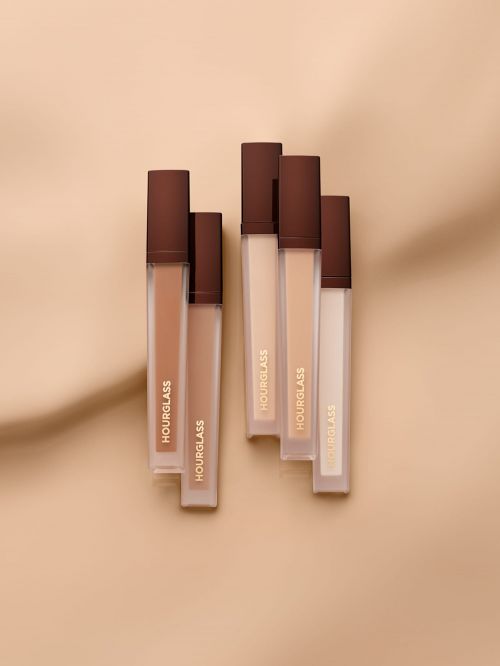 Hourglass brand cosmetics arranged on a tan surface with shadows, showcasing makeup for beauty and personal care products.