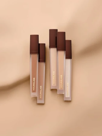 Hourglass brand cosmetics arranged on a tan surface with shadows, showcasing makeup for beauty and personal care products.
