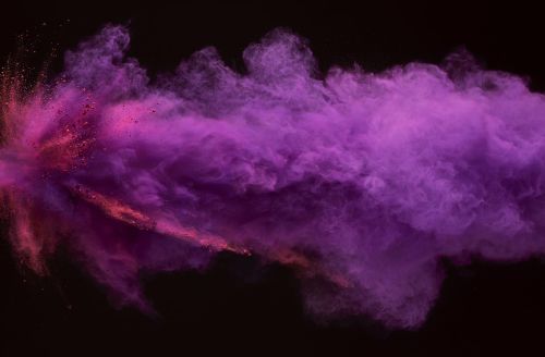 An abstract explosion of vibrant pink and purple powder against a stark black backdrop, creating a dynamic visual effect.