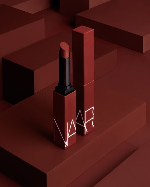 NARS lipstick on a red-brown surface, showcasing beauty and cosmetics in a minimalist composition with geometric shapes in the background.