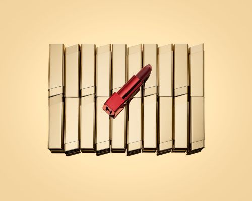 Close-up shot of an open red lipstick tube resting on a collection of closed gold lipstick tubes, creating a visually striking makeup arrangement.