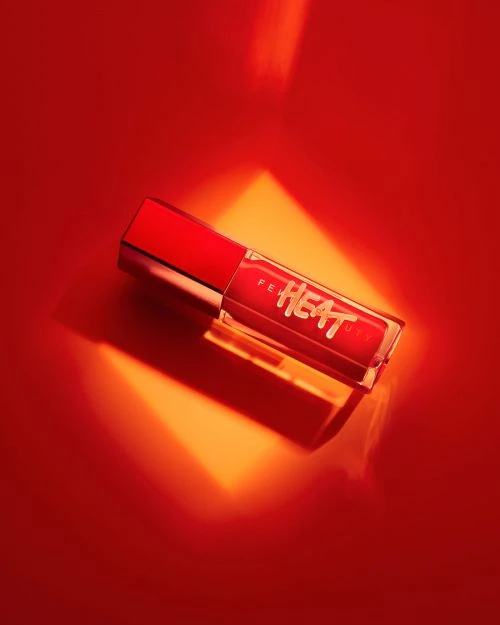 Close-up of red Fenty Heat lip gloss tube on a vibrant red background with spotlight effect highlighting the product details.