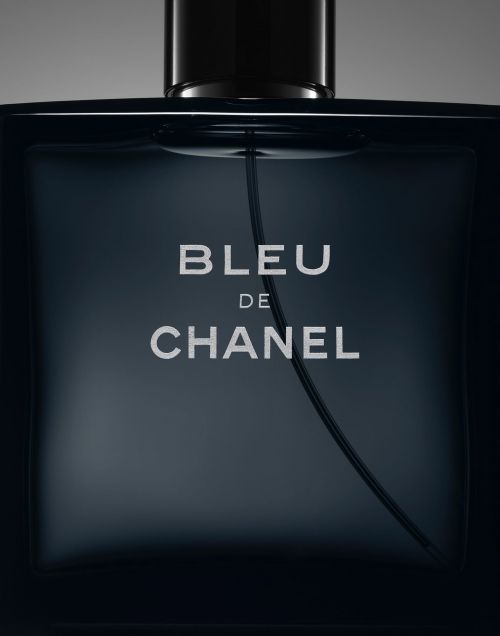 Close-up of a bottle of Bleu de Chanel men's cologne, featuring the brand name prominently on its dark, square-shaped glass container.