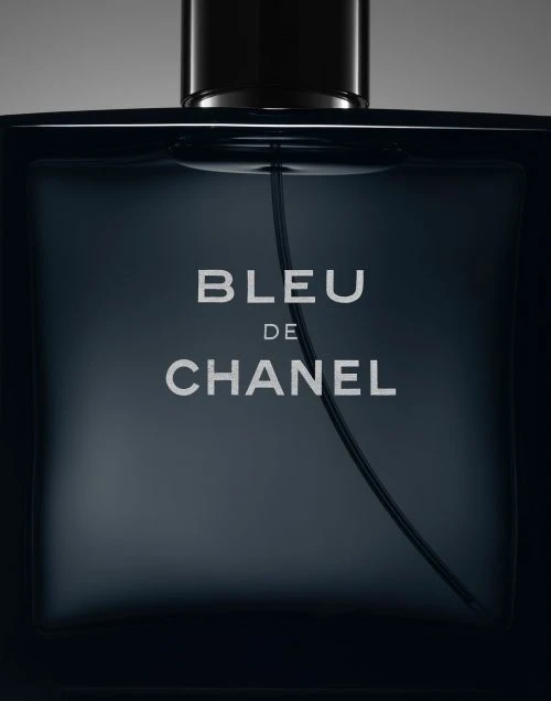 Close-up of a bottle of Bleu de Chanel men's cologne, featuring the brand name prominently on its dark, square-shaped glass container.