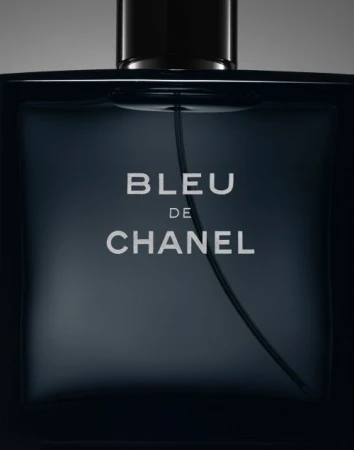 Close-up of a bottle of Bleu de Chanel men's cologne, featuring the brand name prominently on its dark, square-shaped glass container.