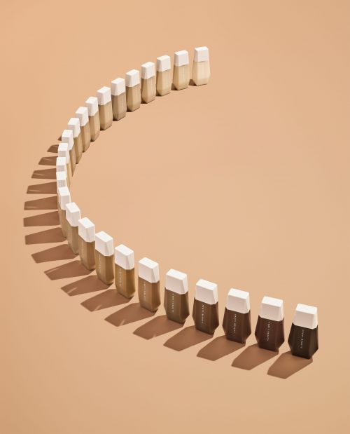 Cosmetic foundation samples arranged in a curved row, featuring a gradient from light to dark shades, against a neutral background.