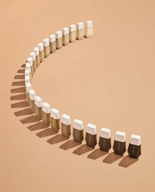 Cosmetic foundation samples arranged in a curved row, featuring a gradient from light to dark shades, against a neutral background.