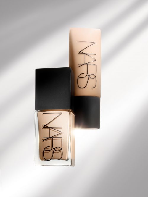 Beauty product shot of two NARS brand foundation bottles in a studio setting with shadow play. The containers are beige and black.