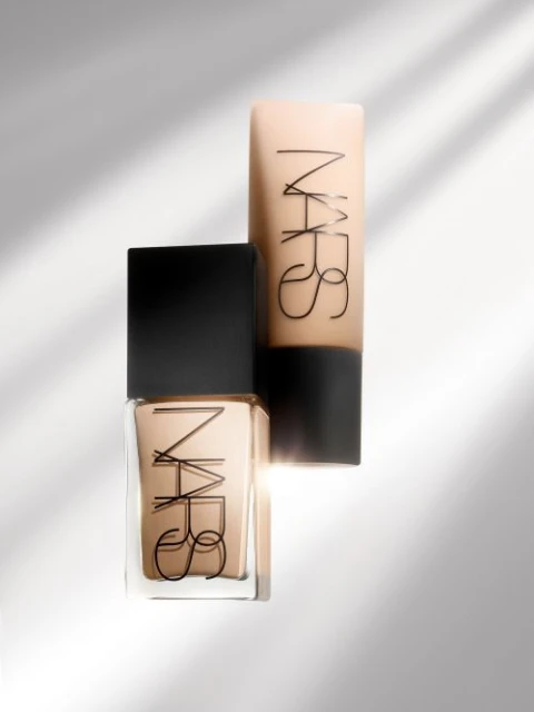 Beauty product shot of two NARS brand foundation bottles in a studio setting with shadow play. The containers are beige and black.