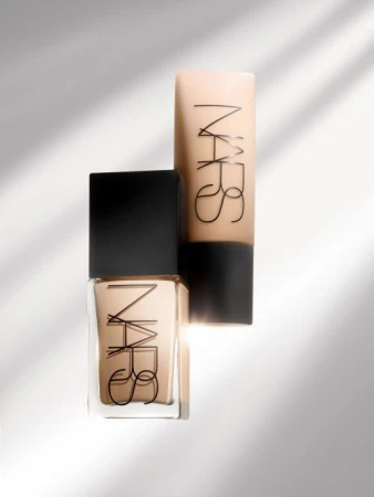 Beauty product shot of two NARS brand foundation bottles in a studio setting with shadow play. The containers are beige and black.
