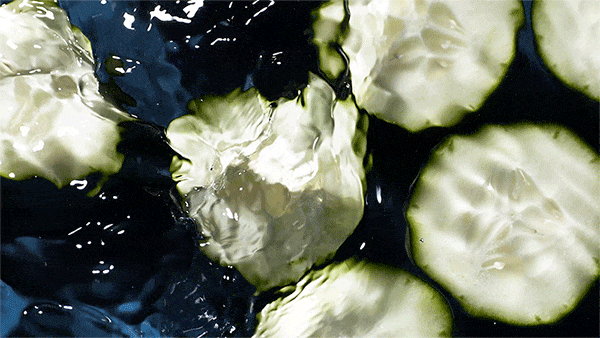 Overhead shot of cucumber slices floating in dark blue water, creating a refreshing and visually appealing food and beverage scene.