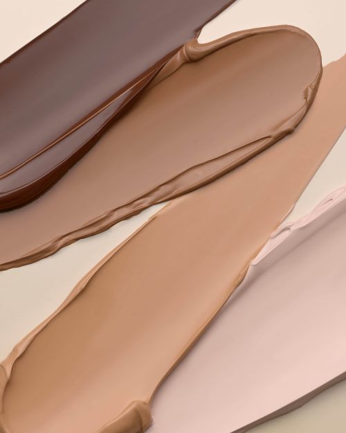 Various shades of liquid foundation are displayed, ranging from dark to light beige, swatched on a neutral background in a beauty shot.