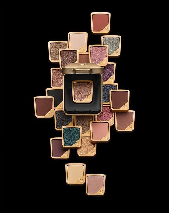 Arrangement of eyeshadow palettes in varied colors with gold trim on a black background, beauty photography for cosmetics and makeup.