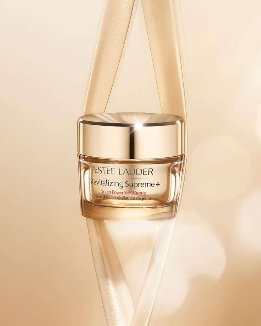 Close-up of Estée Lauder Revitalizing Supreme+ Youth Power Soft Creme jar with light tan ribbon on a light tan background.