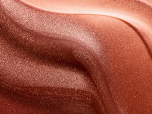 Abstract close-up of shimmering, light-reflecting brown and bronze cosmetic product texture with a swirling, wavy pattern.