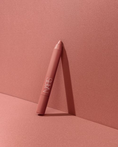 NARS lipstick crayon standing against a monochromatic coral-pink background in a beauty product shot. Makeup and cosmetic photography.