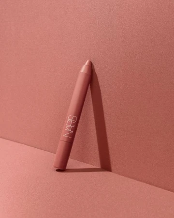 NARS lipstick crayon standing against a monochromatic coral-pink background in a beauty product shot. Makeup and cosmetic photography.