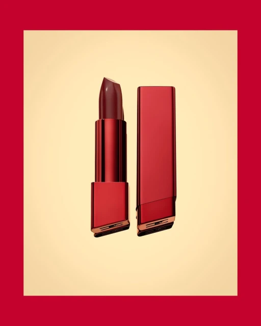 A red lipstick tube is displayed alongside its cap, both positioned on a pale yellow backdrop with a wide red border.