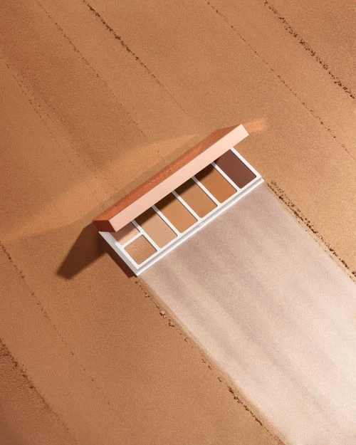 Makeup palette of neutral and brown eyeshadows displayed against a textured tan background, showcasing beauty product packaging.