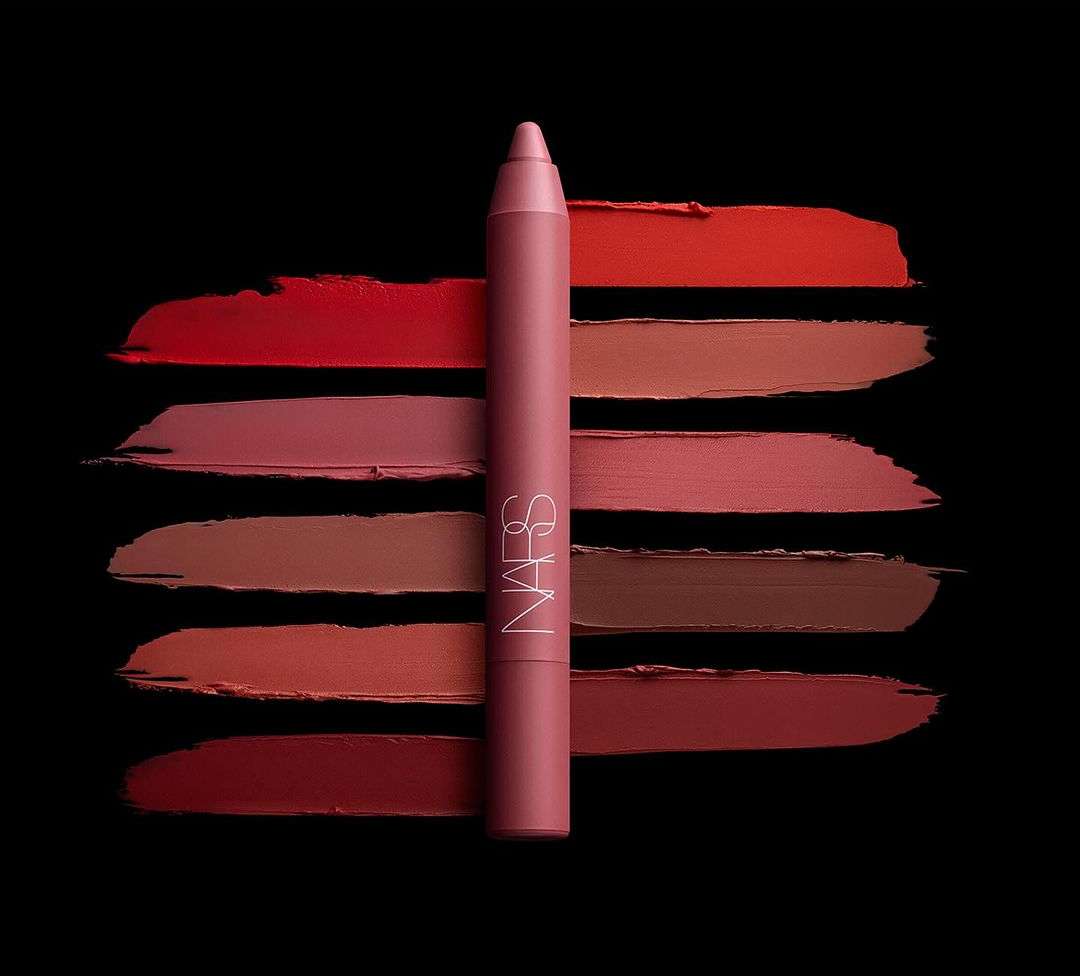 NARS lipstick crayon and swatches of different shades of lipstick in a row on a black background. Beauty and makeup advertisement.