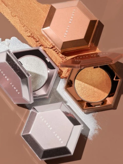 Three open and closed hexagon-shaped containers of shimmery Fenty Beauty highlighter sit against bronze and silver shimmery powder swatches.