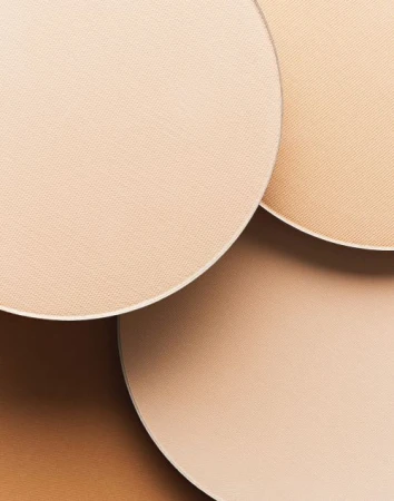 Close-up of circular cosmetic powder compacts in various neutral tones, displaying a range of shades for makeup application.