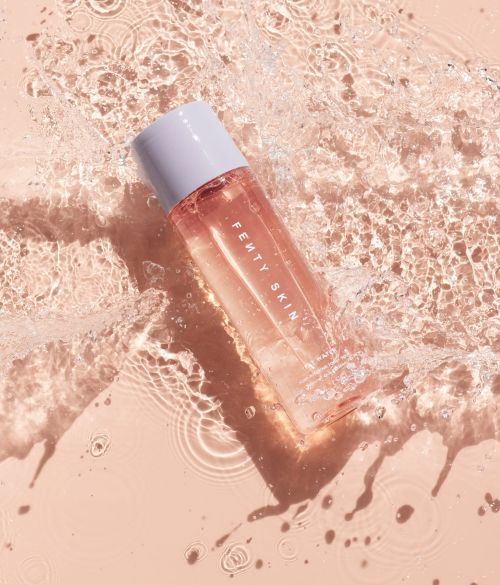 Fenty Skin skincare bottle with white cap surrounded by water splashes, creating a refreshing and clean beauty aesthetic.