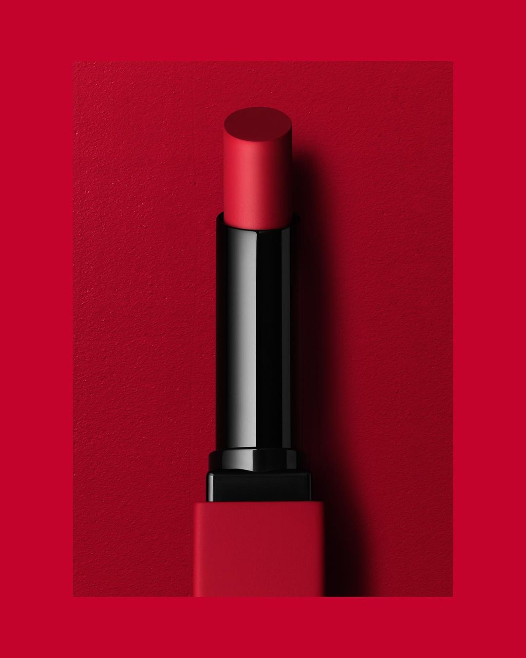 Red lipstick tube on a matching red background, clean beauty shot, minimal composition, cosmetic product photography.