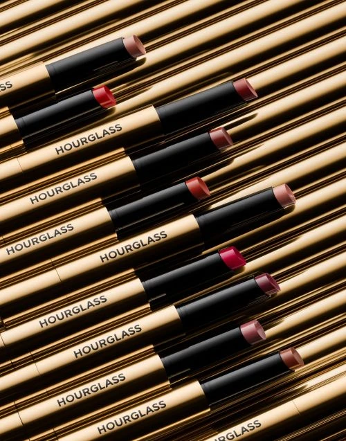 Hourglass lipsticks lined up on a gold surface in a beauty product photography arrangement, displaying a variety of shades and luxury branding.
