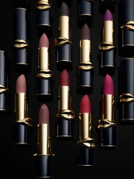 Close-up arrangement of multiple black and gold lipstick tubes with molded lip motifs on a dark reflective surface